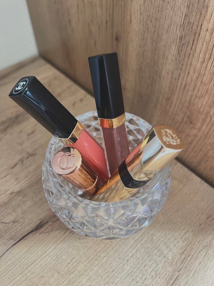 Four luxury lipsticks in a crystal holder on a wooden surface.