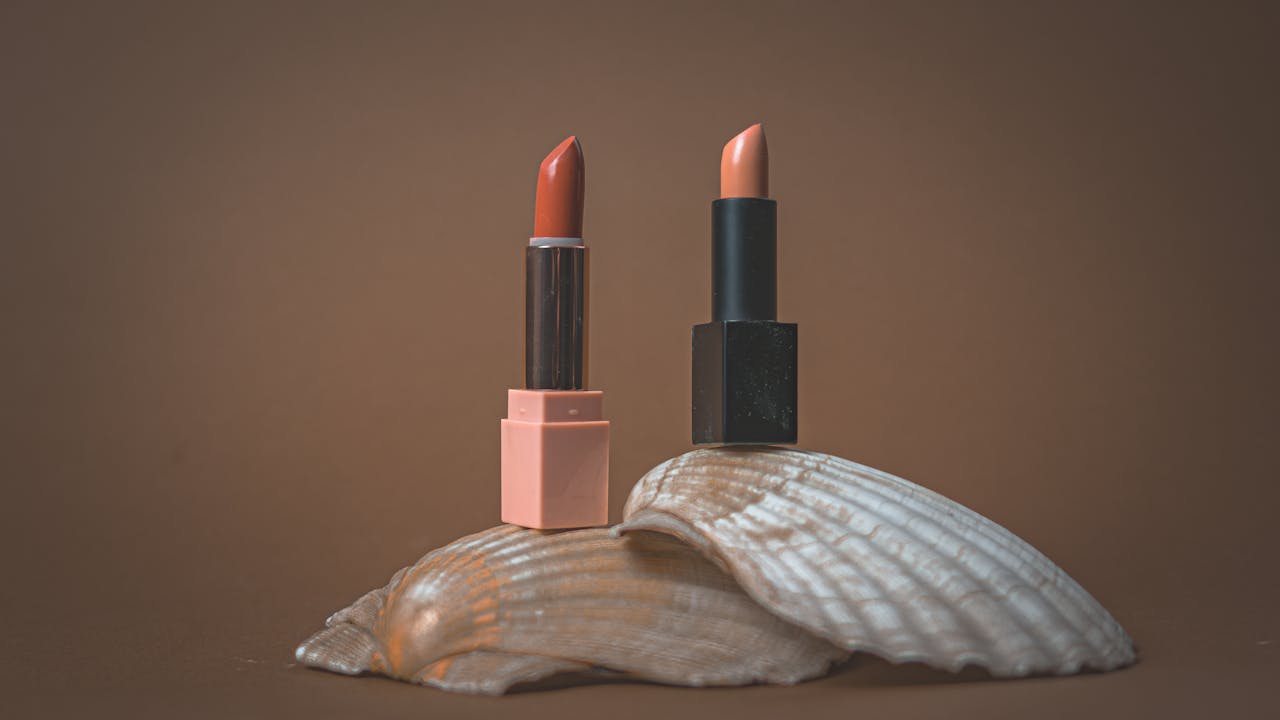 Two elegant lipsticks displayed on a seashell with a minimalist, earthy backdrop.