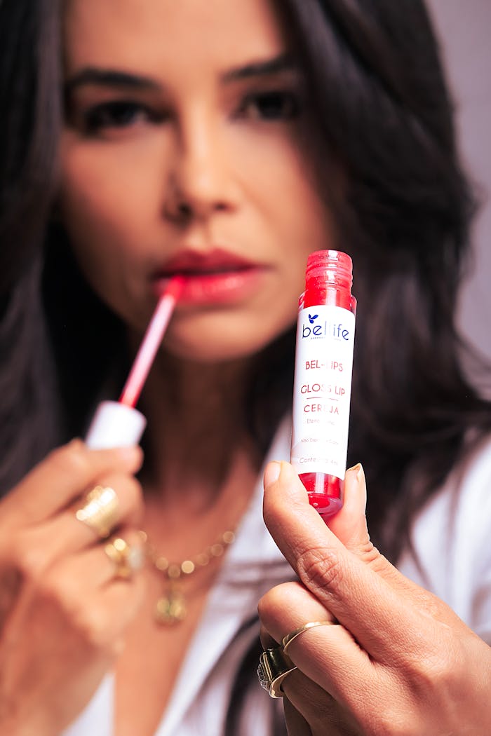 Close-up of a woman applying red lip gloss with focus on the product tube.